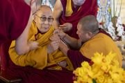 Помощники закрепляют микрофон на одеянии Его Святейшества Далай-ламы перед началом церемонии вручения степеней геше-лхарамбы на площадке Калачакры. Бодхгая, штат Бихар, Индия. 3 января 2024 года. Фото: Тензин Чойджор